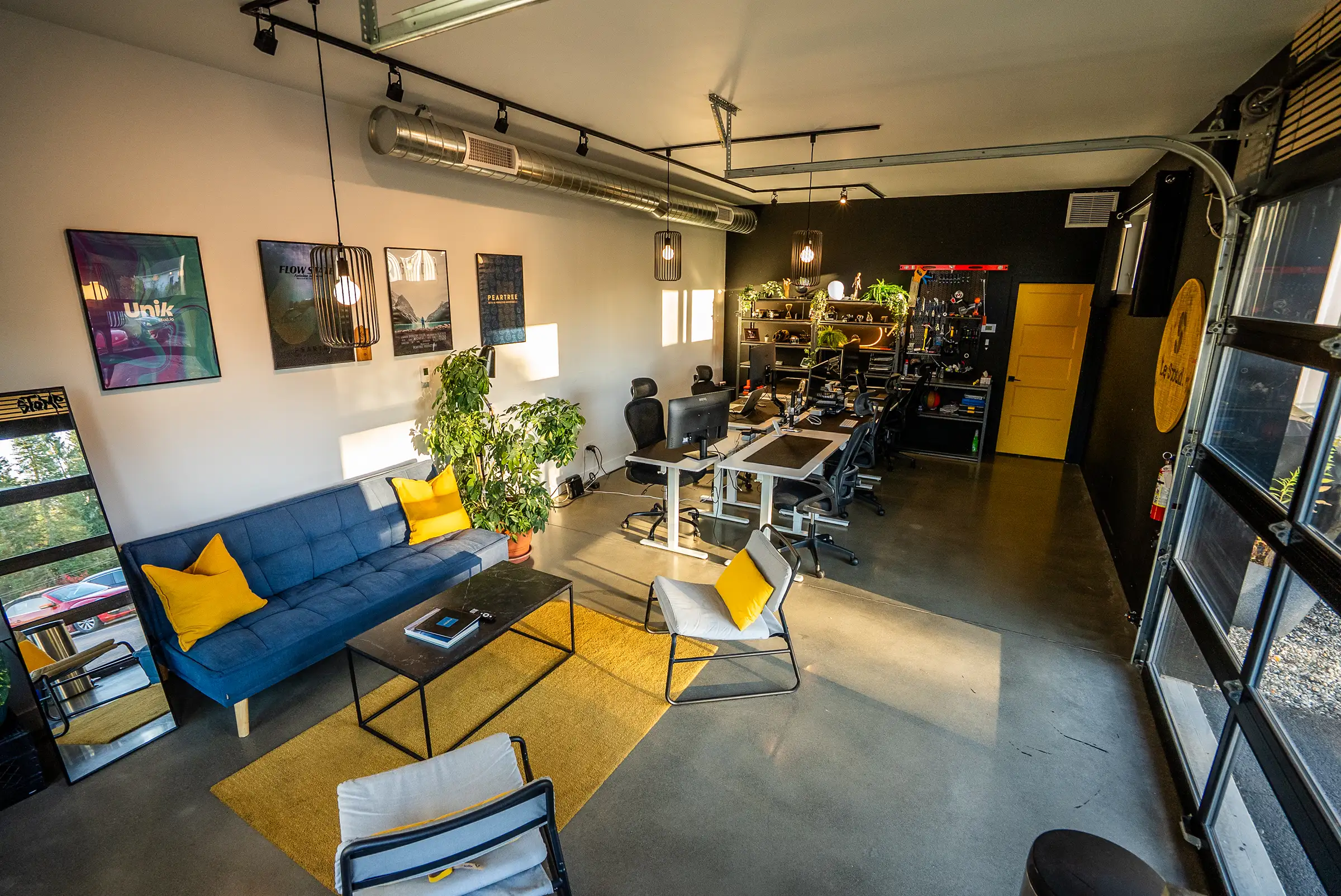 Le local d'Unik Studio au Stoud, à Bromont : le salon au divan bleu, les postes de travail et la porte de garage vitrée