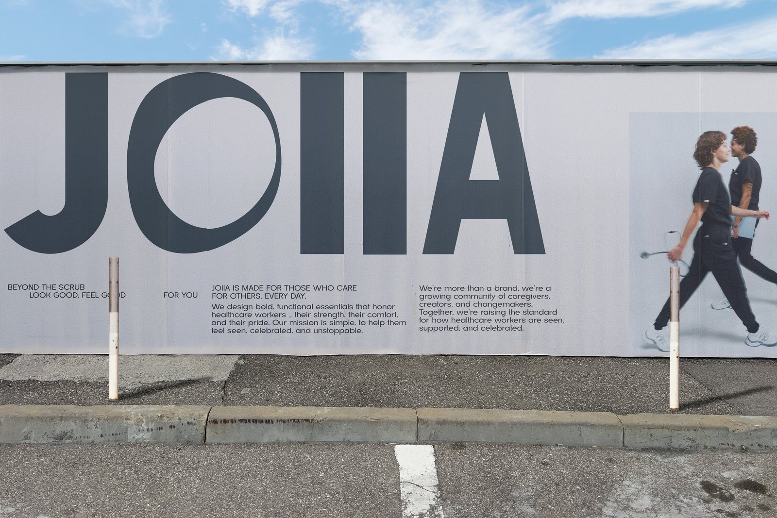 Palissade de rue de Joiia Wear : le logo Joiia en très grand, un court texte et deux travailleurs de la santé en uniformes
